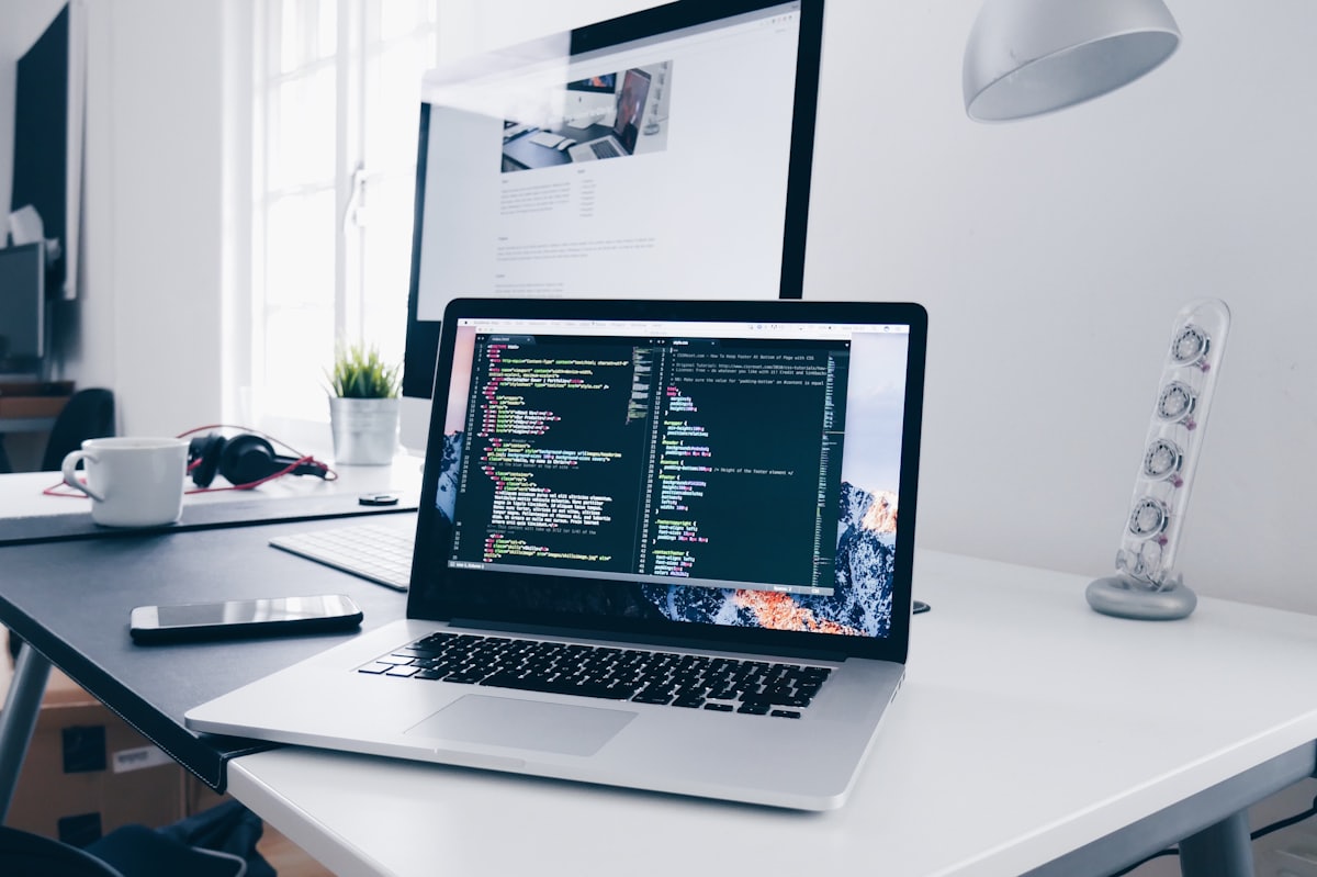 A laptop and external monitor showing code in a bright workspace